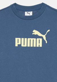 Kék pamut környakú póló, nagy sárga "PUMA" logóval és egy ugró puma grafikával. Puha tapintású, laza fit kialakítással.