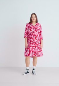 Εντυπωσιακό φόρεμαwrap σε κόκκινες και λευκές αποχρώσεις με σχέδιο, 3/4 μαν�ίκια και ζώνη στη μέση, συνδυασμένο με μαύρα αθλητικά παπούτσια μέχρι τον αστράγαλο. Λεπτό ύφασμα, σε μήκος μέχρι το γόνατο.