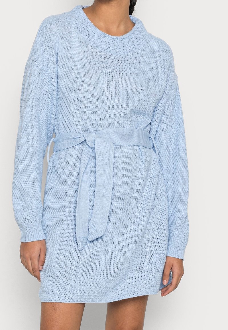 Robe en tricot bleu clair à manches longues, coupe décontractée, avec ceinture à nouer à la taille. Tissu texturé avec un motif de point lâche.