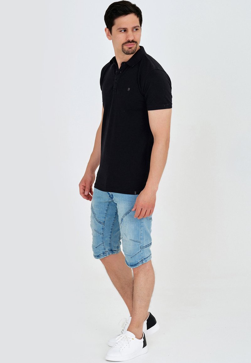 Tricou polo negru cu guler, asortat cu pantaloni scurți din denim albastru deschis, cu cusături contrastante. Modelul poartă adidași albi cu accente negre.