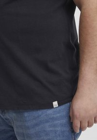 Sort bomulds T-shirt med korte ærmer, der har et lille logomerke ved kanten. Båret med blå denim jeans.