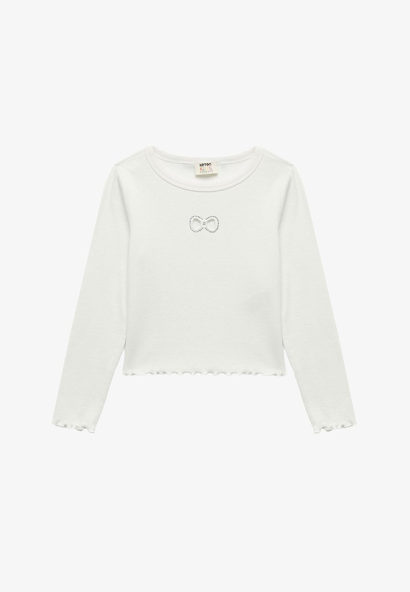 Crop top blanc à manches longues avec un ourlet volé, présentant un petit motif de nœud en strass sur la poitrine. Matière en coton doux.