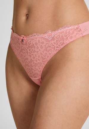 Mutandine in pizzo rosa morbido con motivo floreale e piccolo dettaglio a fiocco indossate sui fianchi e sull'addome inferiore di una persona.