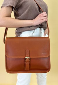 Brun læder messenger taske med en flad forflap, spænde lukning og justerbar rem. Glat tekstur med syede detaljer.