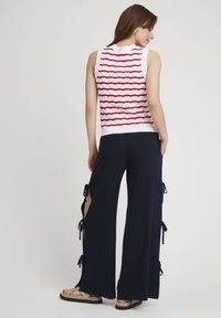 Haut sans manches blanc avec des rayures horizontales rouges ; associé à un pantalon taille haute bleu marine avec des fentes sur les côtés et des nœuds décoratifs.