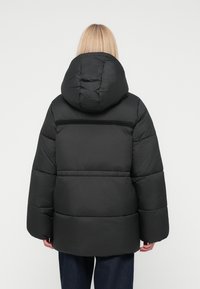 Black puffer jacket with a hood, featuring a puffy design, wide sleeves, and a clean finish. Textured fabric with a smooth exterior.