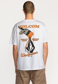 T-shirt en coton blanc avec un imprime graphique audacieux au dos, comprenant des éléments orange et noir avec les textes "VOLCOM" et "Workwear".
