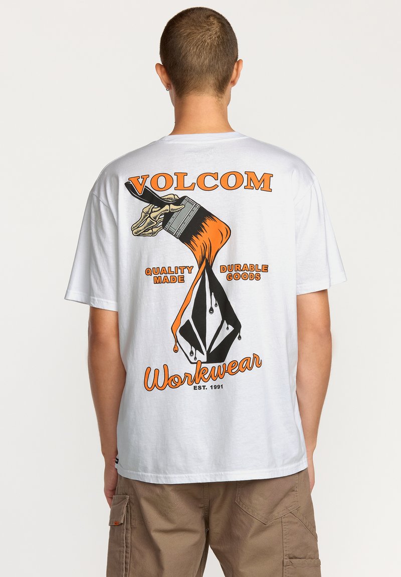 T-shirt en coton blanc avec un imprime graphique audacieux au dos, comprenant des éléments orange et noir avec les textes "VOLCOM" et "Workwear".