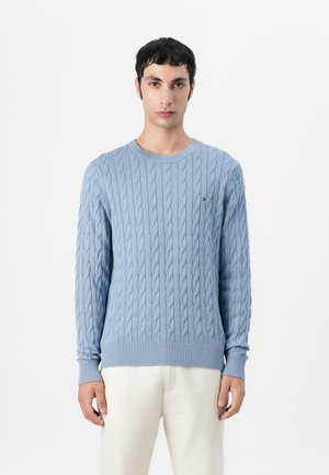 Pulover din lână cu un model tricotat în culori albastre deschise, cu decolteu rotund și manșete cu model în care. Prezintă un logo mic pe piept. Textură netedă și design ajustat.