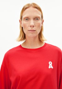 Rood katoenen T-shirt met een ronde hals, voorzien van een wit geborduurd bewustwordingslint op het linkerborstgebied.