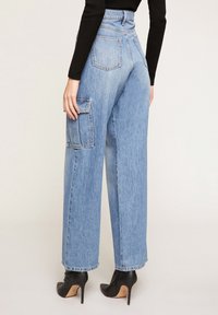 Jeansy w kolorze niebieskim z wysokim stanem, szerokie, z łatką na lewej nodze, z postrzępionymi brzegami i luźnym krojem.