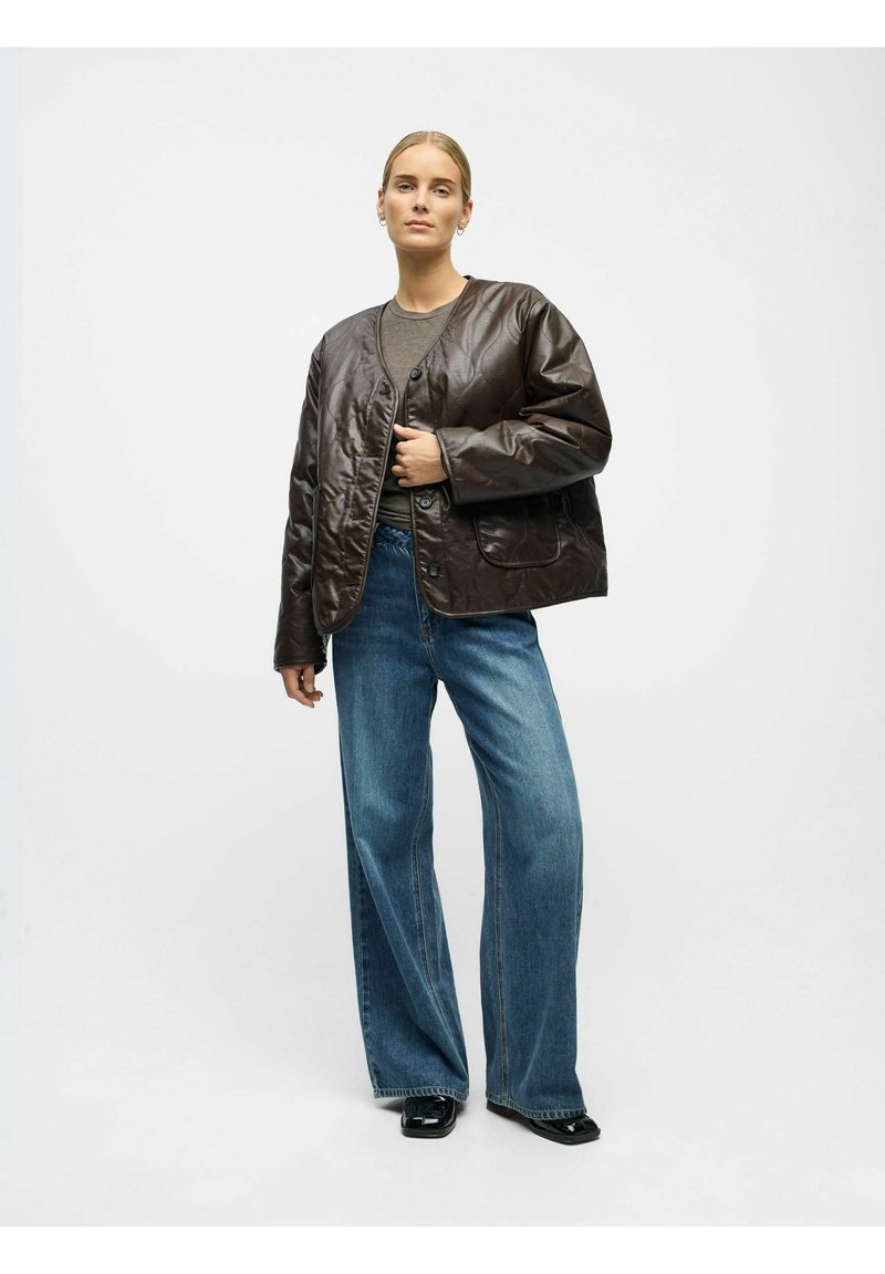 Braune gesteppte Lederjacke mit Knopfleiste, abgerundetem Kragen und Seitentaschen, kombiniert mit weit geschnittenen blauen Jeans.