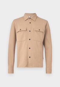 Veste-chemise beige à manches longues avec boutons-pression noirs et deux grandes poches à rabat devant sur fond blanc.