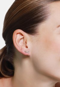 Silberne Ohrstecker in Form einer kleinen Schleife. Elegantes, poliertes Metall mit einem schlichten Design, das sanfte Kurven und abgerundete Kanten aufweist.