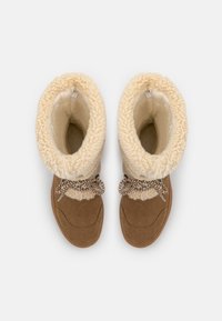 Botas de tobillo de ante marrón con forro de piel sintética color crema, presentan un diseño de solapa y cordones con patrón.
