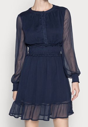 Laivansinis mekko, jossa on pitkät läpikuultavat hihat, nappisuljenta edessä, joustava vyötärö ja kerroksellinen rypytyshelma. Pehmeä, kevyt materiaali.