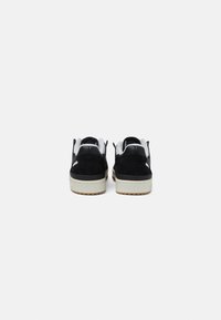 Zwarte suede sneakers met witte accenten, ronde neus, platte rubberen zool en gevoerde kraag, met een schoon ontwerp vanaf de achterkant bekeken.