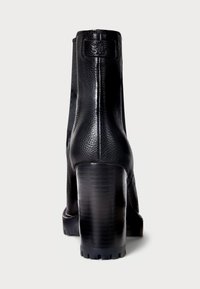 Črne usnjene gležnjarje z strukturirano površino, visokim blokastim peto in gumijastim podplatom s podrobnostmi profila. Zadnji pogled na čevlje.