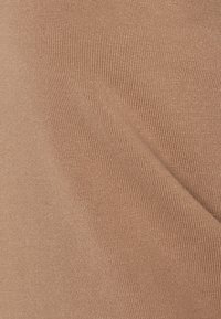 Detailní záběr na béžovou pletenou tkaninu ukazující jemnou ribovanou strukturu a subtilní diagonální záhyb.