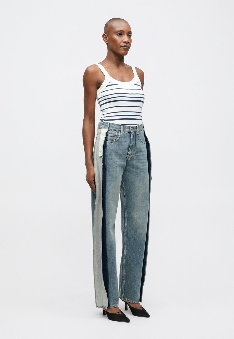 Randig vit tanktopp kombinerad med vida denimjeans med flerfärgad lapptäcksteknik i blått, grått och kontrasterande sömmar. Svarta klackar.