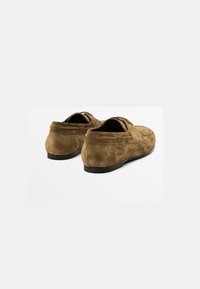Bruine suède schoenen met een lage profiel, ronde neus en minimale stiksels. Zwarte rubberen zolen bieden contrast en grip.