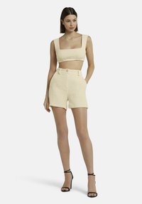 Crème-kleurige twee-delige outfit met een crop top met vierkante halslijn en hoge taille shorts met zijzakken en knoopdetails. Soepele textuur.