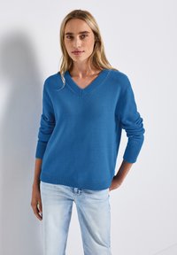 Pull bleu à col en V avec des accents côtelés, manches longues et coupe décontractée. Assorti à un jean en denim bleu clair.