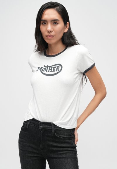 Λευκό κοντομάνικο μπλουζάκι με μαύρο ριγέ γιακά, με τη λέξη "MOTHER" σε έντονα γράμματα. Συνδυασμένο με σκούρο τζιν, δείχνοντας ένα καθημερινό στυλ.