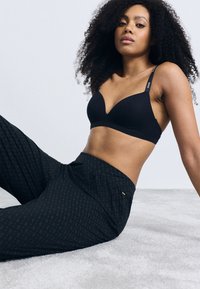 Sorte trådløs BH med dyp utringning og justerbare stropper, kombinert med tettsittende svarte mønstrede bukser. Myk tekstur, avslappet passform.