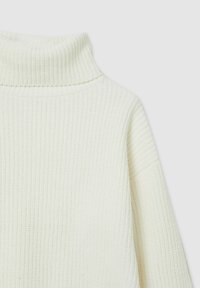Pull encolure roulée couleur crème avec texture côtelée et coupe décontractée. Il présente un col haut et replié ainsi qu'une couture d'épaule tombante.