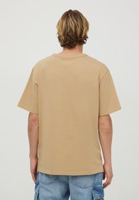 T-shirt beige overdimensionato con collo a manica corta realizzato in tessuto morbido. Maniche corte, vestibilità rilassata e texture liscia. Nessun marchio o motivo visibile.