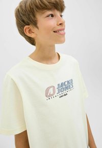 Svijetložuta pamučna majica s kratkim rukavima, s višebojnim logotipom koji sadrži natpis "JACK & JONES" i srodni tekst.