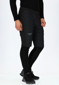 Zwarte gevoerde shorts met een gladde textuur en elastische tailleband, gecombineerd met zwarte thermoleggings en zwarte sport schoenen.