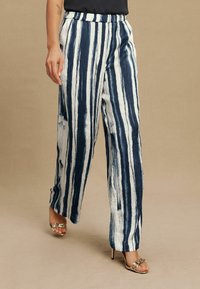 Wide-leg trousers feature vertical navy and white stripes, made from a textured fabric. The waistband is elastic, providing comfort.