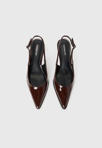 Scarpe con tacco slingback in vernice marrone scuro a punta, con soletta nera e cinturini laterali con fibbia, viste dall'alto su uno sfondo bianco.
