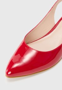 Piros, lakkbőrből készült, hegyes orrú slingback sarokcipő sima felülettel, világos bézs belsővel és minimalista dizájnnal.