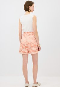 Shorts à motifs floraux dans des tons pêche avec une texture lisse, présentant une taille haute et un ourlet retroussé. Associés à un haut sans manches blanc.