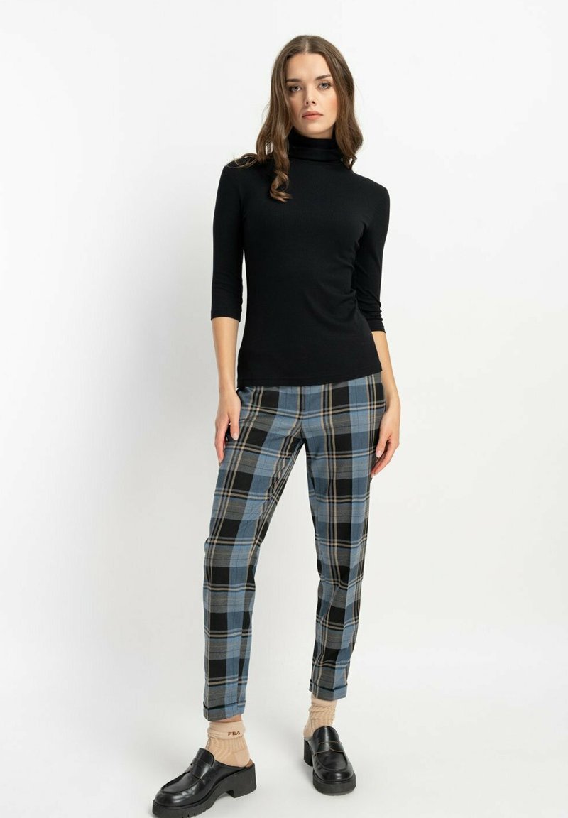 Czarny golf z rękawami o długości trzy czwarte, w połączeniu z niebieskimi i czarnymi spodniami w kratę. Modelka nosi czarne buty na platformie.