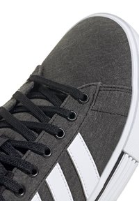 Baskets en toile grise avec des rayures blanches, des lacets noirs et des œillets métalliques. La semelle est blanche avec un design texturé.