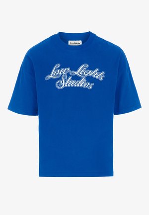 T-shirt bleu à manches courtes avec texte cursif blanc « Low Lights Studios » centré sur le devant et une petite étiquette de marque au niveau de l'encolure.