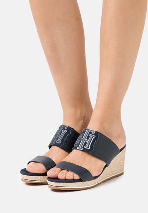 Mørkeblå kilehæle i marinefarve med stropper af stof med logo, en bred frontrem og vævet jute-detalje på kile-sålen.