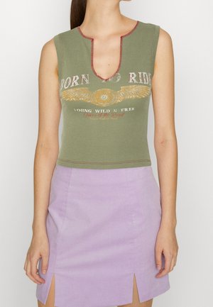 Ärmelloses olivgrünes Crop-Top mit rotem Saum und geflügeltem Emblem, kombiniert mit einem hoch taillierten lavendelfarbenen Rock mit seitlichen Schlitzen.