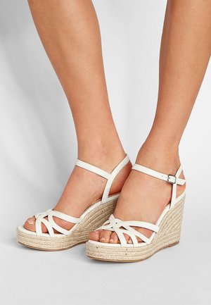 White strappy wedge sandals with a woven rope sole, featuring crisscross design on the toe and adjustable ankle strap for fit.