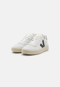 Hvite lær sneakers med perforert design, beige såle, og svart V-logo på siden. Har hvite lisser og subtile detaljer på tungen.