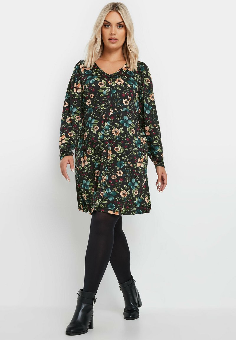 Pitkähihainen musta kukkamekko, jossa on värikkäitä kukkia, V-pääntie ja keräyksi�ä olkapäillä, yhdistettynä mustiin sukkahousuihin ja nilkkureihin.