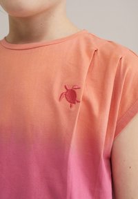 Rausvos ombre spalvos medvilnės marškinėliai su apvaliu kaklu ir trumpomis rankovėmis. Išskirtinė detalė: siuvinėta vėžlio logo ant krūtinės.
