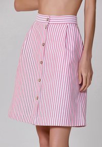 Jupe A-line rayée rose et blanche avec un devant à boutons, un design plissé et une taille à rayures horizontalement. Comprend cinq boutons.