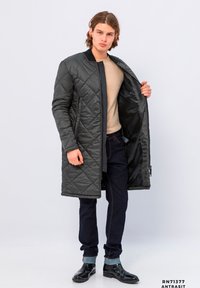 Gepolsterter, dunkelgrauer, gesteppten Mantel mit Reißverschluss, offenem Vorderteil und Rippkragen, kombiniert mit dunkelblauen Jeans und schwarzen Stiefeln.