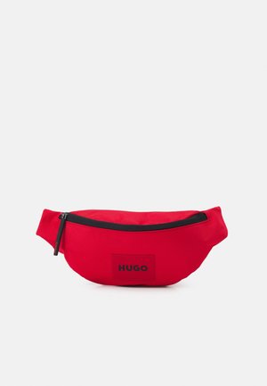 Banane en tissu rouge avec fermeture éclair noire et écusson logo "HUGO" à l'avant, présentée sur un fond clair uni.