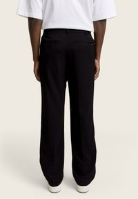 Pantaloni negri ajustați cu un design drept, având buzunare la spate și o textură netedă. Purtați cu o cămașă albă și pantofi casual.